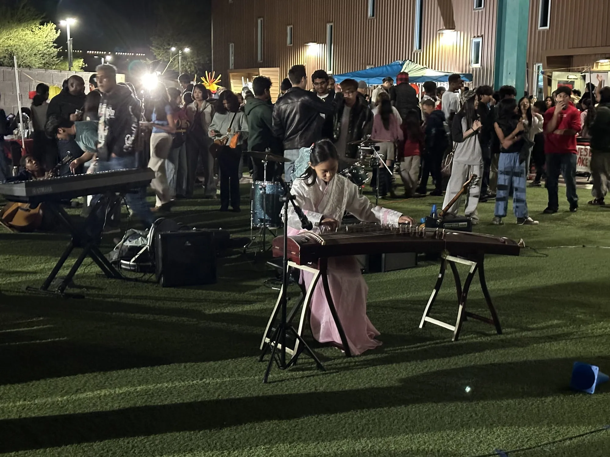 A student in traditional dress plays the guzheng as a crowd gathers behind her